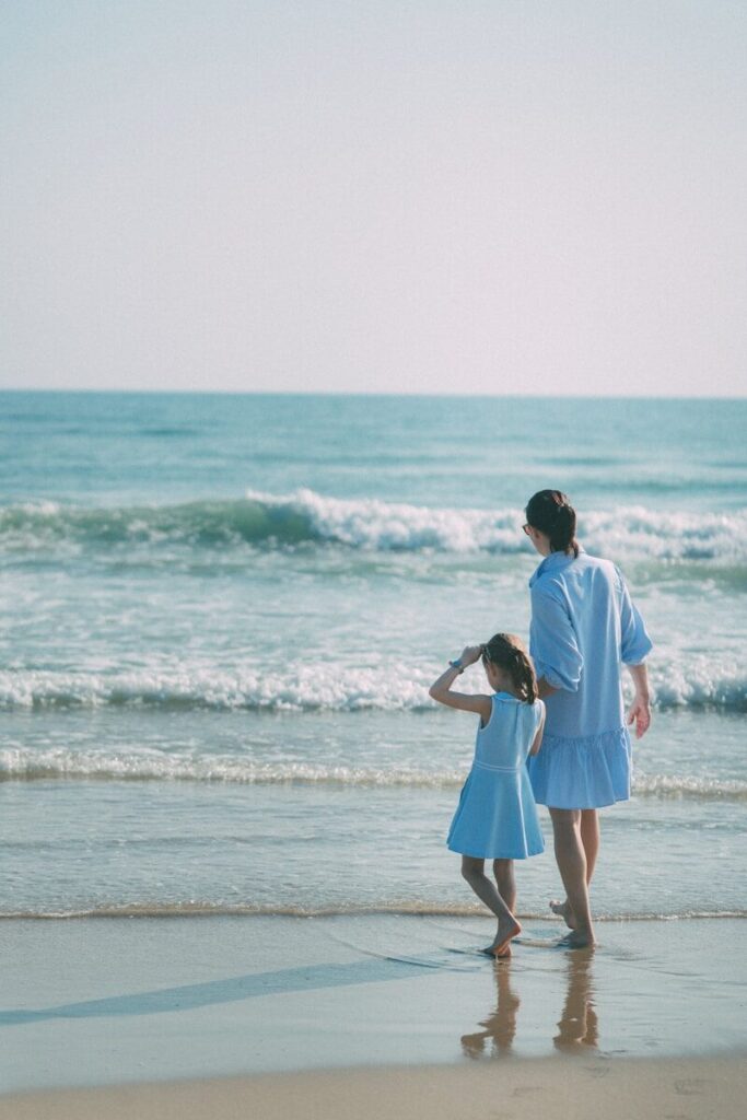 Mother and daughter watch waves on a sunny beach.
