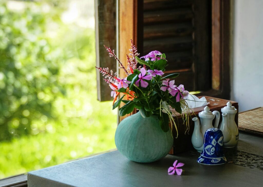 Flowers in a vase sit near an open window.