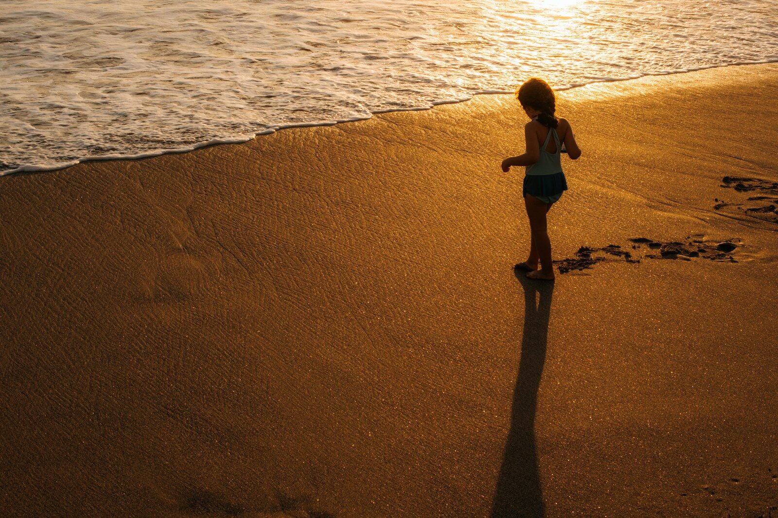A child plays on a sandy beach at sunset.
