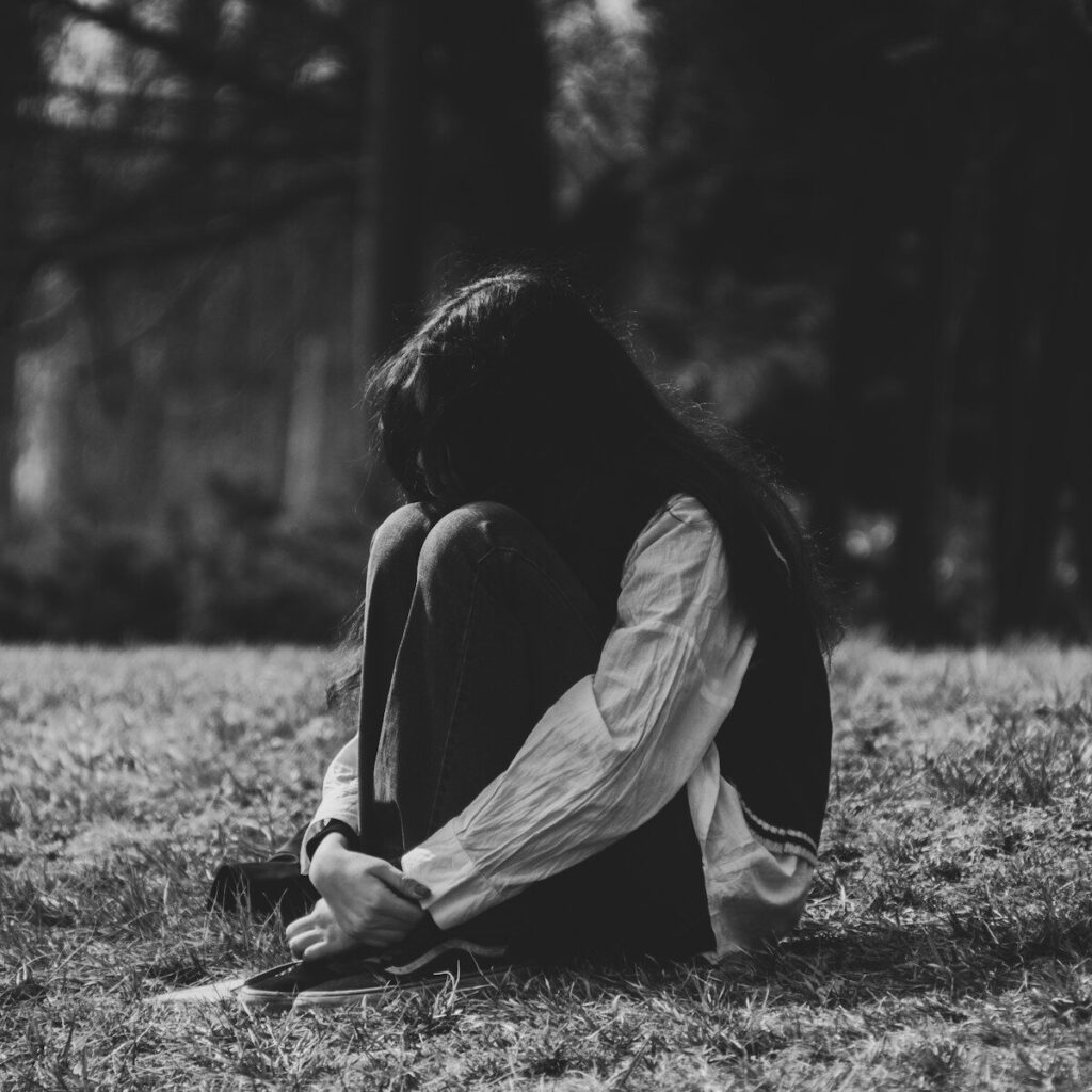 A person sits curled up on grassy ground.