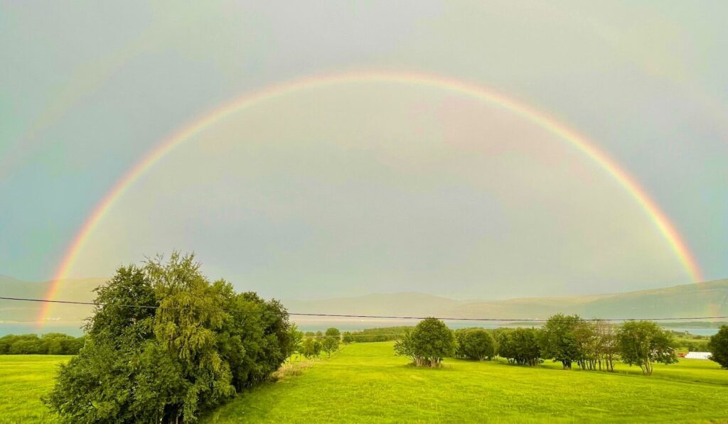 A vibrant rainbow arches over a green landscape.